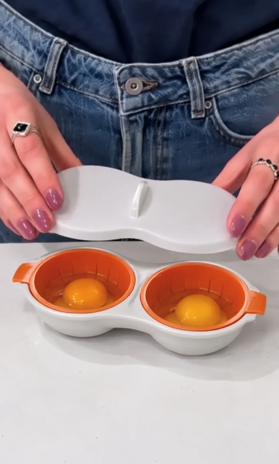 Manos sosteniendo la tapa del pochador con dos huevos crudos en las canastillas naranjas