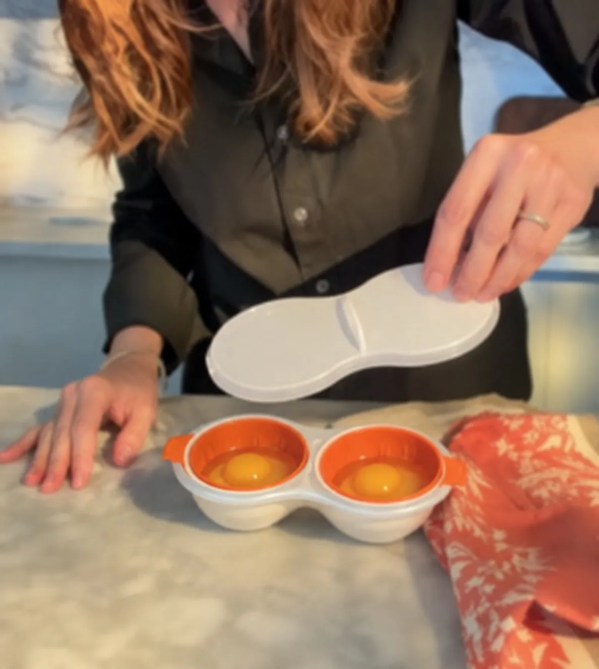Persona colocando la tapa sobre el pochador con dos huevos en las canastillas