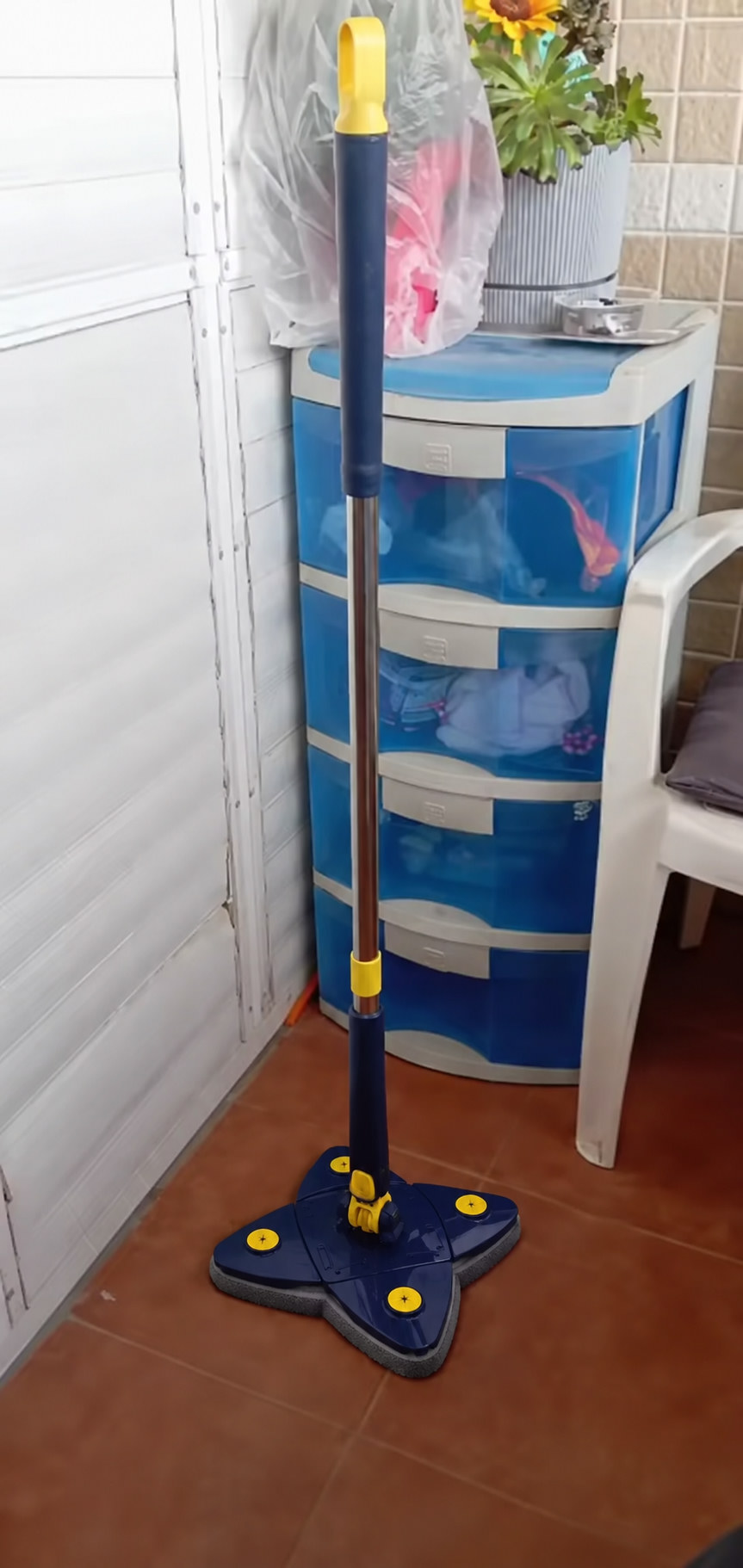 Trapero triangular 360° de pie sobre piso de baldosa, con mango azul y amarillo