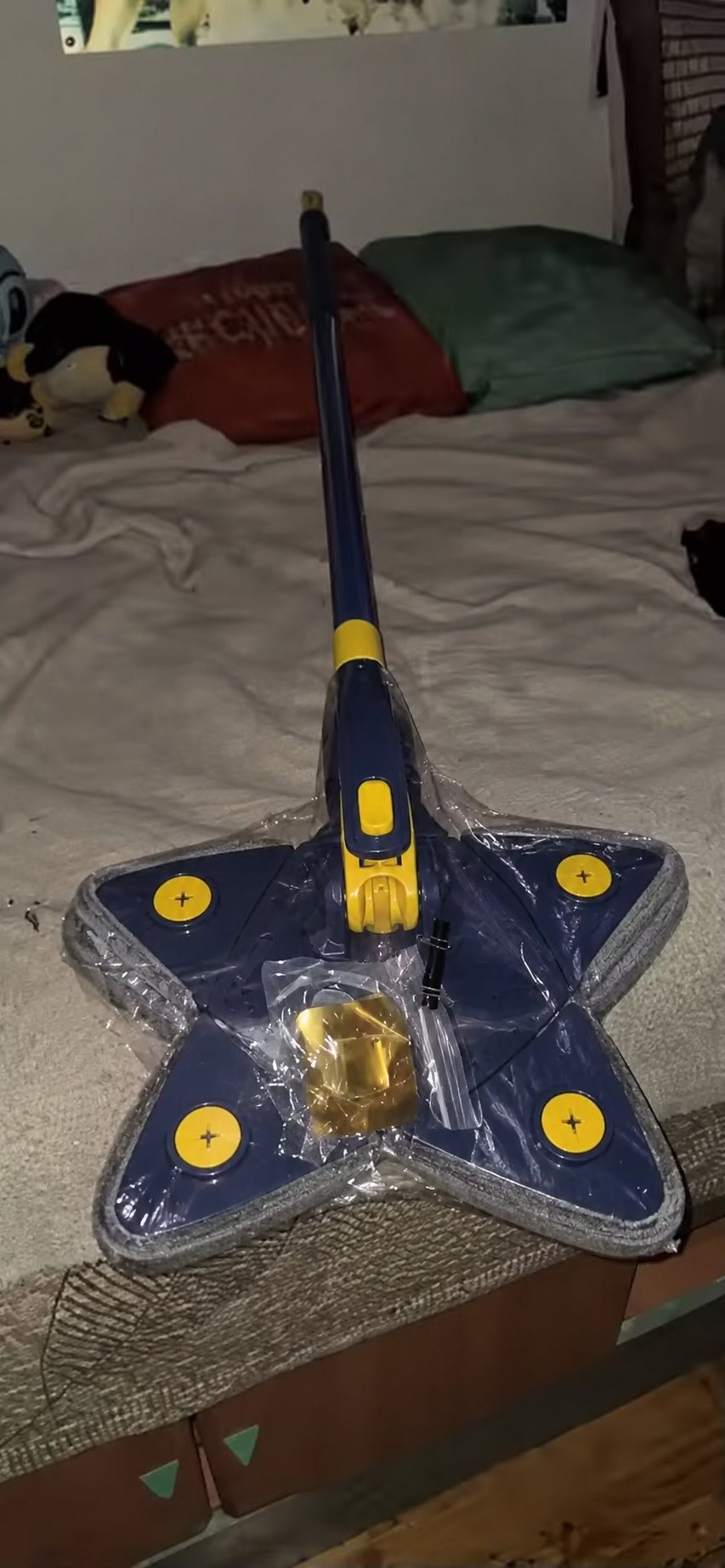 Trapero triangular 360° recién recibido, con mango azul y cabezal de 4 puntas sobre la cama